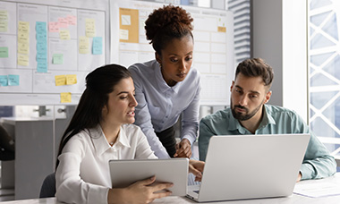 group of people in discussion while looking at laptops, with project boards in background