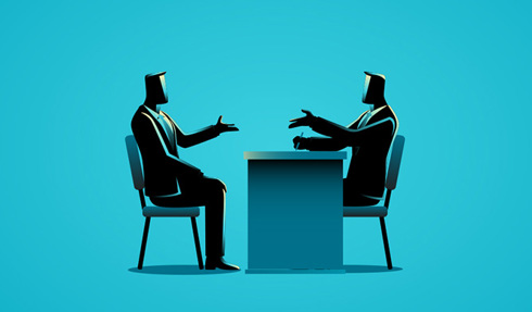 Two people talking at a desk.