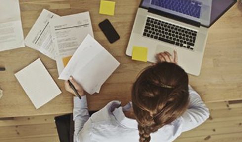 Woman working on a laptop surrounded by papers and sticky notes.