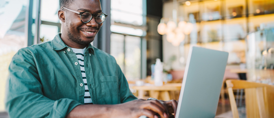 A smiling man types on a laptop in a restaurant setting.