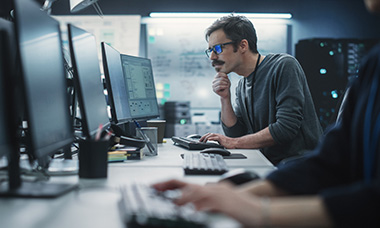 man coding at desk facing multiple monitors