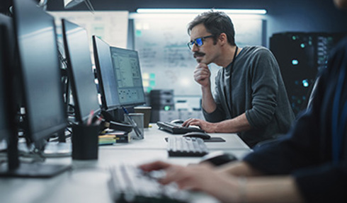 person looking at multiple monitors and typing on keyboard
