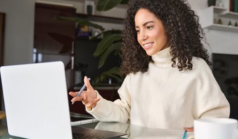 Woman working on a lap top and holding a pen.