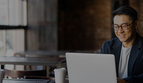 person working on a laptop at a table in a modern office or café setting, with large windows and coffee cups in the foreground