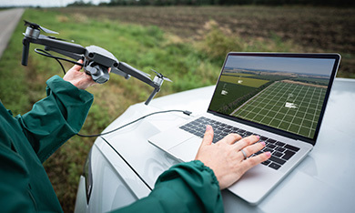 Person holding a drone while typing on a laptop outdoors