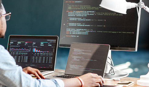 person coding at desk with multiple monitors